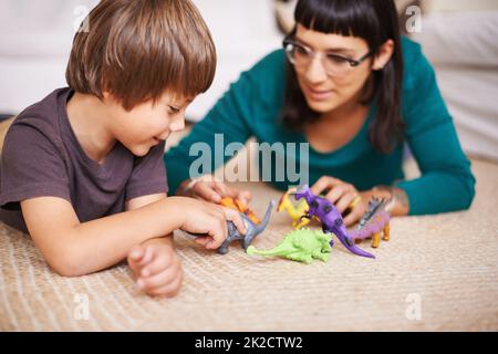 Dinosaurier spielen mit Mama. Ausgeschnittene Aufnahme einer Mutter und ihres Sohnes, die mit Spielzeug-Dinosauriern spielen. Stockfoto