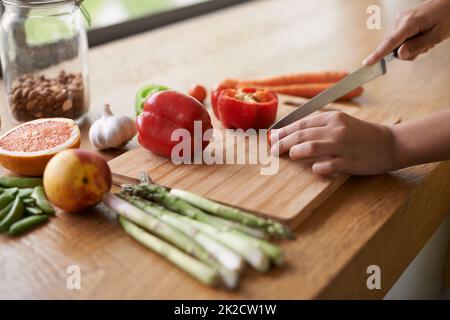 Bereiten Sie einen frischen Leckerbissen zu. Nahaufnahme eines zugeschnittenen Bildes von einer Frau, die auf einem Schneidebrett Lebensmittel zubereitete. Stockfoto