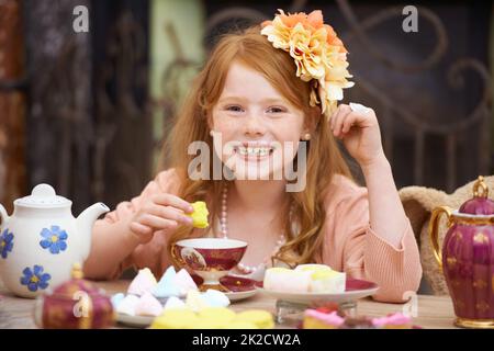 Möchten Sie etwas Tee? Ein niedliches Mädchen mit rotem Kopf spielen verkleiden sich und mit einer Tee-Party. Stockfoto