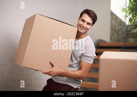 Ich kann es kaum erwarten, in mein neues Hotel zu kommen. Ein glücklicher junger Mann, der verpackte Pappkartons in seinem Haus bewegt. Stockfoto