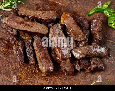 Geröstetes Stück Rinderribeye auf einem braunen Schneidebrett in Stücke geschnitten. Gut gemacht. Appetitliches Steak, Blick von oben Stockfoto