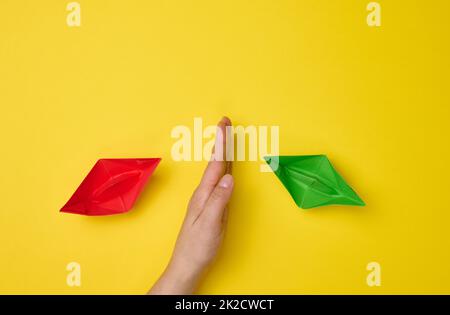 Weibliche Hand zwischen Papierbooten auf gelbem Hintergrund, das Konzept der Versöhnung der Parteien, die Suche nach Kompromissen. Die Rolle des Verhandlungsführers im dialog Stockfoto