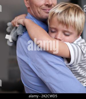 Erschöpft nach einem unterhaltsamen Tag. Ein reifer Vater kommt von der Arbeit nach Hause und umarmt seinen erschöpften kleinen Jungen. Stockfoto