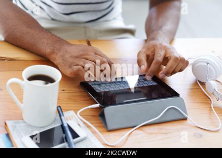 Aktualisierung des Blogs seines Unternehmens. Beschnittene Ansicht eines afroamerikanischen Mannes, der an seinem Schreibtisch an einem digitalen Tablet arbeitet. Stockfoto