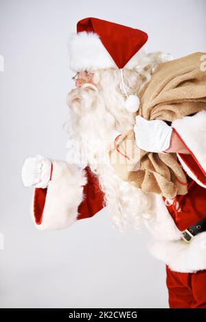 Santas auf dem Weg. Der Weihnachtsmann läuft mit einem Sack Geschenke auf dem Rücken - isoliert auf Weiß. Stockfoto