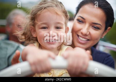 Wir machen den Alltag zu einem Abenteuer. Porträt eines kleinen Mädchens, das auf dem Schoß ihrer Mutter sitzt. Stockfoto