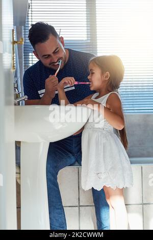 Es ist ihre tägliche Gewohnheit. Eine kleine Aufnahme von einem Vater und einer Tochter, die ihre Zähne am Waschbecken im Badezimmer zusammenputzten. Stockfoto