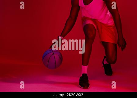 Nehmen Sie Ihre Position in den Besitz. Rot gefilterte Aufnahme eines nicht erkennbaren Sportlers, der mit einem Basketball im Studio posiert. Stockfoto