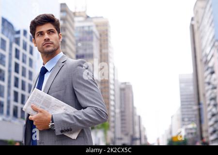 Die Unternehmenswelt gut aussehen zu lassen. Ein hübscher junger Geschäftsmann mit einer Zeitung, der durch die Stadt läuft. Stockfoto