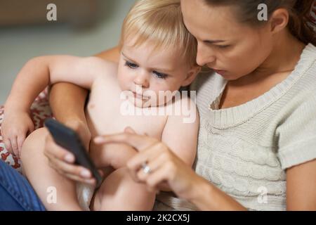 Schau dir das an Eine Mutter zeigt ihrem Jungen etwas auf ihrem Handy. Stockfoto