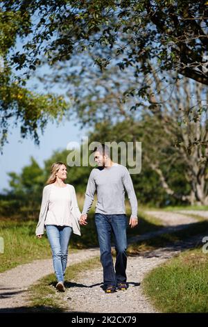 Es ist ein perfekter Tag für die Liebe. Ganzkörperaufnahme eines jungen Paares, das Hand in Hand in einem Park läuft. Stockfoto