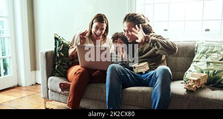 Ich grüße den Rest der Familie. Aufnahme eines fröhlichen jungen Paares und ihres Sohnes, die mit ihren Verwandten über einen Laptop ein Videogespräch führen, während sie zu Hause auf einem Sofa sitzen. Stockfoto