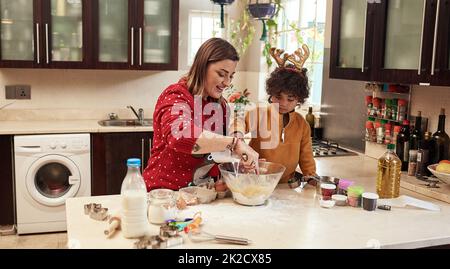 Weihnachtssnacks zubereiten. Eine kurze Aufnahme einer fröhlichen jungen Frau und ihres Sohnes, die während der weihnachtszeit zu Hause in der Küche zusammen Kekse backen. Stockfoto