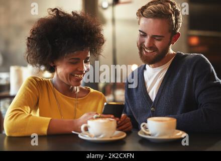 Teilen Sie die Dinge, die sie zum Lächeln bringen. Aufnahme eines jungen Paares, das ein Mobiltelefon zusammen auf einem Kaffeetrinken benutzt. Stockfoto