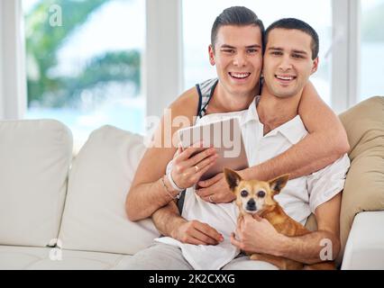 Waren eine glückliche Familie. Porträt eines liebevollen schwulen Paares, das sich mit seinem Hund auf dem Sofa entspannt. Stockfoto