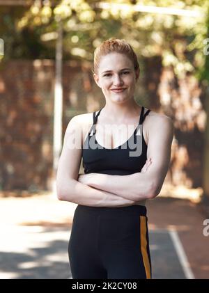 Vertrauen auf den Platz. Ein beschnittenes Porträt einer attraktiven jungen Sportlerin, die mit gefalteten Armen auf dem Basketballfeld steht. Stockfoto