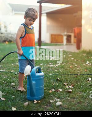 Die Natur pflegen. Aufnahme eines kleinen Jungen, der eine Gießkannenflasche mit einem Schlauch füllte. Stockfoto