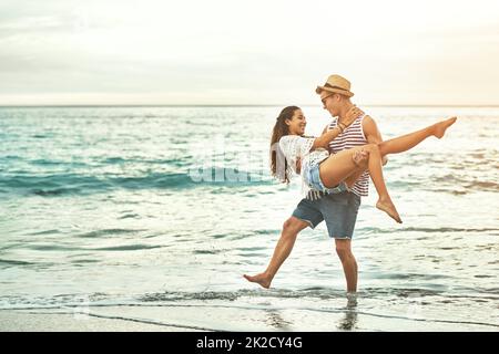 Ich lasse dich nie gehen. Die ganze Aufnahme eines liebevollen jungen Paares, das seine Zeit am Strand genießt. Stockfoto