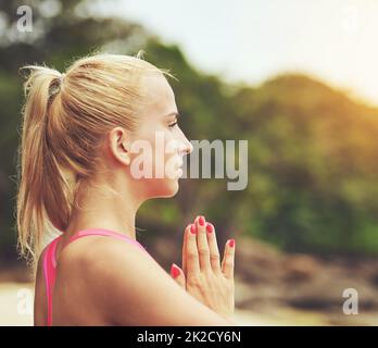 Einatmen von frischer Meeresluft. Aufnahme einer fokussierten jungen Frau, die am Strand Yoga macht. Stockfoto