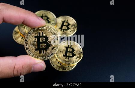 Menschliche Finger, die Bitcoins auf schwarzem Hintergrund halten Stockfoto