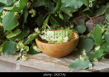 Lindenblüten mit Blättern in Holzschüssel auf Holztisch. Tilia Stockfoto