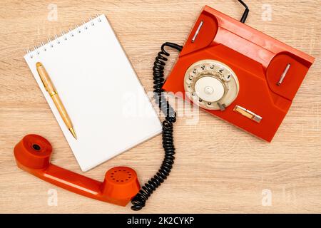 Orangefarbenes Drehtelefon und leeres Notizbuch auf Holzhintergrund Stockfoto