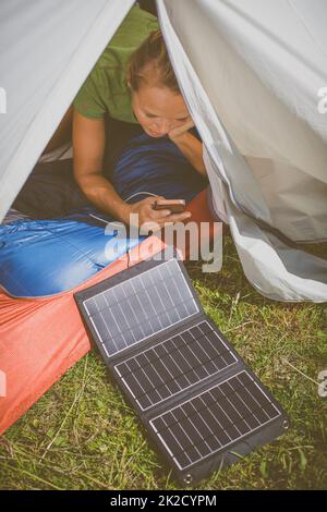 Handy wird während einer Fahrt im Freien mit einem Solarladegerät in einem Zelt aufgeladen Stockfoto