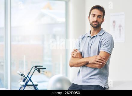 Für die Gesundheit meiner Patienten. Beschnittenes Porträt eines männlichen Physiotherapeuten, der mit gefalteten Armen in seinem Büro sitzt. Stockfoto