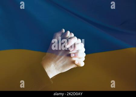 Nahaufnahme der ukrainischen Flagge mit betenden Händen Stockfoto