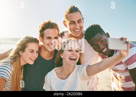 Feiern Sie die Sommersaison mit einem Selfie. Aufnahme einer glücklichen Gruppe von Freunden, die zusammen Selfies am Strand machen. Stockfoto