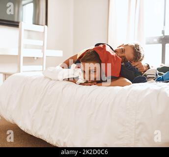 Einen weiteren dummen Moment gemeinsam zu teilen. Porträt zweier kleiner Brüder, die zu Hause auf einem Bett unter einem Wäschestapel liegen. Stockfoto