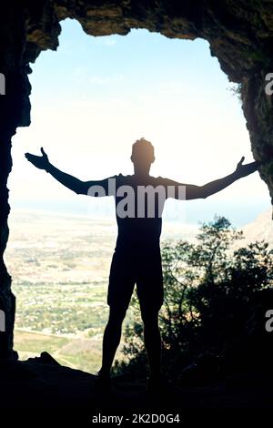 Oben ist es heller. Rückansicht eines jungen Mannes, der mit ausgestreckten Armen auf einem Berg steht. Stockfoto