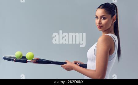 Denken Sie, Sie haben das Zeug dazu. Beschnittenes Porträt einer attraktiven jungen Tennisspielerin, die vor grauem Hintergrund im Studio posiert. Stockfoto