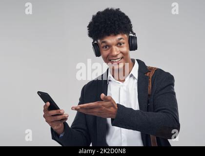 Klingt für mich wie ein Siegerlied. Studioaufnahme eines jungen Geschäftsmannes mit Smartphone und Kopfhörer vor grauem Hintergrund. Stockfoto