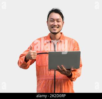 Der Chefmechaniker in einer orangefarbenen Uniform hält einen Laptop. Mit den Daumen nach oben stehend. Porträt mit Studiolicht. Stockfoto