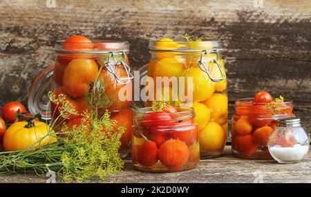 Eingelegte Tomaten in Töpfen auf hölzernen Tisch. Tomaten fermentiert Prozess Gläsern Vielfalt - rot, gelb, orange Stockfoto