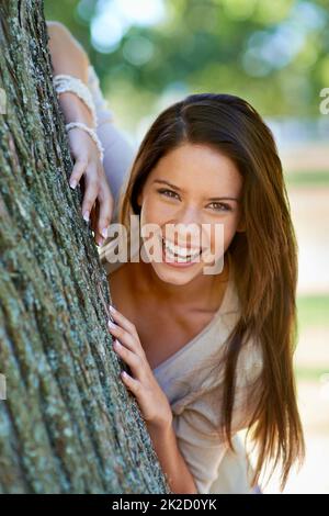 Frei, ich selbst zu sein. Porträt einer schönen jungen Frau, die hinter einem Baum im Park steht. Stockfoto