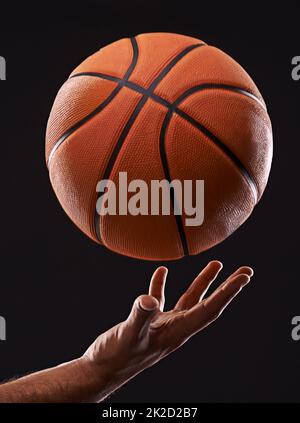 Zeit, dein Spiel zu verbessern. Zugeschnittenes Bild einer mans-Hand, die einen Basketball vor einem schwarzen Hintergrund hält. Stockfoto