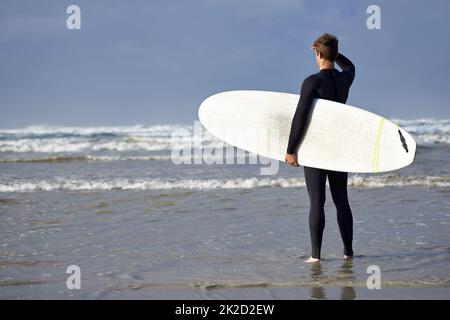 Bereit für die Wellen. Aufnahme eines jungen Mannes, der kurz vor dem Surfen steht. Stockfoto