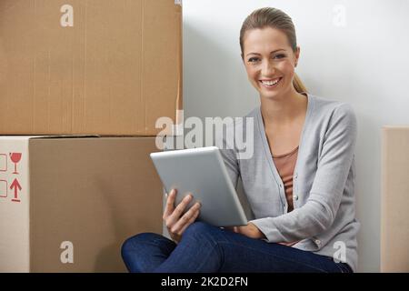 Sind in Bewegung, aber die Arbeit hört nicht auf. Eine junge Frau, die an ihrem digitalen Tablet arbeitet, während sie neben Boxen sitzt. Stockfoto