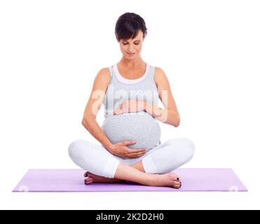 Ruhe und Gelassenheit für Mutter und Baby. Eine junge werdende Mutter meditiert friedlich, während sie auf Weiß isoliert ist. Stockfoto