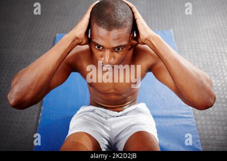 Schwitzen Sie. Aufnahme eines fokussierten Mannes, der Sit-ups auf einer Matte im Fitnessstudio macht. Stockfoto