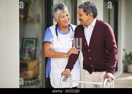 Sie haben so große Fortschritte gemacht. Ausgeschnittene Aufnahme einer Krankenschwester, die mit ihrem älteren Patienten und seinem Spaziergänger draußen spazieren geht. Stockfoto