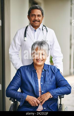 Ihr Komfort und ihre Fürsorge sind ihr verpflichtet. Porträt einer älteren Frau im Rollstuhl, die von einem männlichen Arzt in einem Altersheim betreut wird. Stockfoto