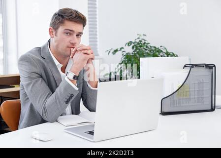 Erwägen, seine nächste Karriere zu bewegen. Ein seriöser junger Geschäftsmann, der an seinem Schreibtisch sitzt und seine Optionen in Betracht zieht. Stockfoto