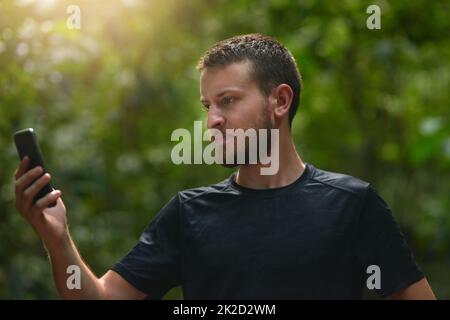 Verloren in einem Dschungel gute Sache youve bekam GPS. Aufnahme eines jungen Mannes, der sein Handy benutzte, während er alleine in einem Dschungel stand. Stockfoto