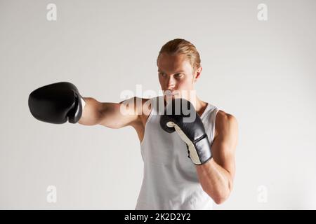 Er nimmt seine Boxkarriere sehr ernst. Ein hübscher junger Boxer, der eine Weste trägt und einen Schlag wirft. Stockfoto