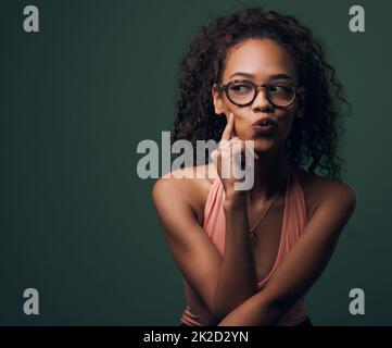 Nicht nur ein hübsches Gesicht. Eine kurze Aufnahme einer attraktiven und skurrilen jungen Frau, die vor grünem Hintergrund im Studio posiert. Stockfoto