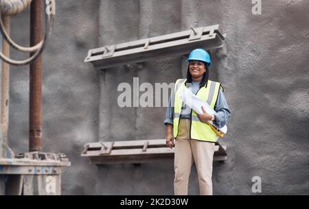 Ich muss sicherstellen, dass die Arbeit erledigt wird. Beschnittenes Porträt einer attraktiven jungen Bauarbeiterin, die auf der Baustelle arbeitet. Stockfoto