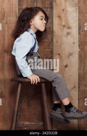 Ich mag meinen Stil Old-School. Aufnahme eines niedlichen kleinen Jungen in altmodischen Overalls, der auf einem Hocker sitzt. Stockfoto